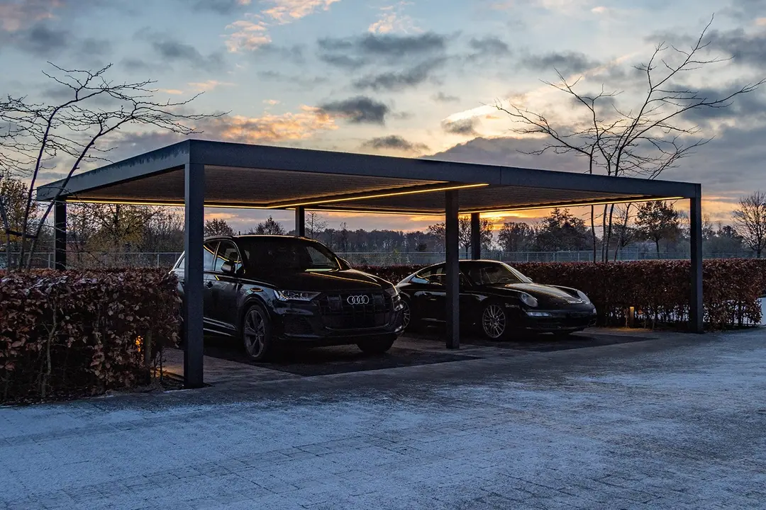Podwójny Carport w kolorze antracytowym o zmierzchu, taśmy LED wzdłuż rynny i krokwi, pod dachem dwa auta, w tle bukowy żywopłot