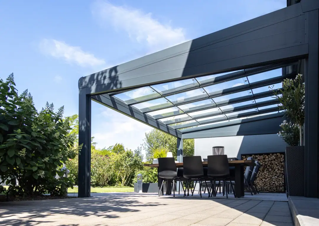 Jadalnia pod Designstyle w kolorze antracytowym, szklany dach z krokwiami widziany od spodu, z boku składowisko drewna