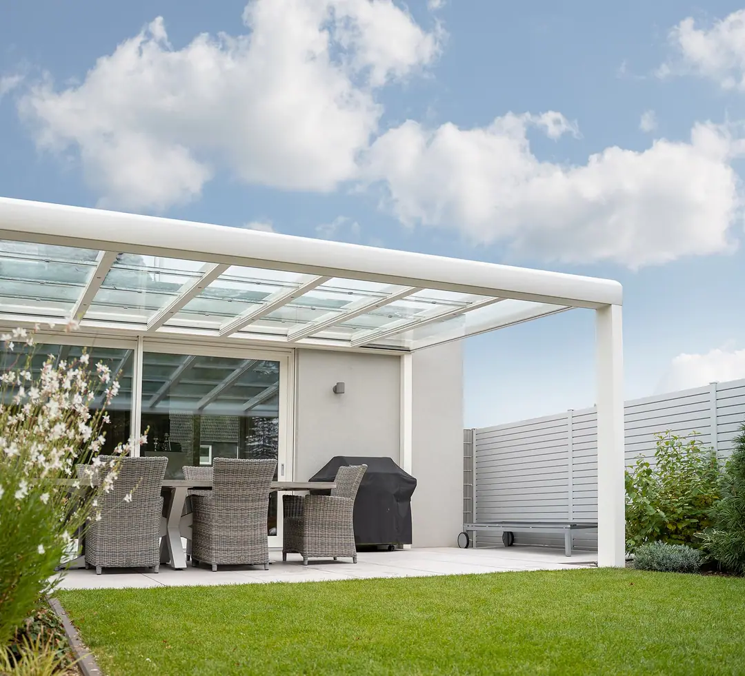 Designstyle w kolorze białym przy jasnym domu, zbliżenie na słupek, rynnę i krokwie nad szkłem, pod dachem jadalnia i grill