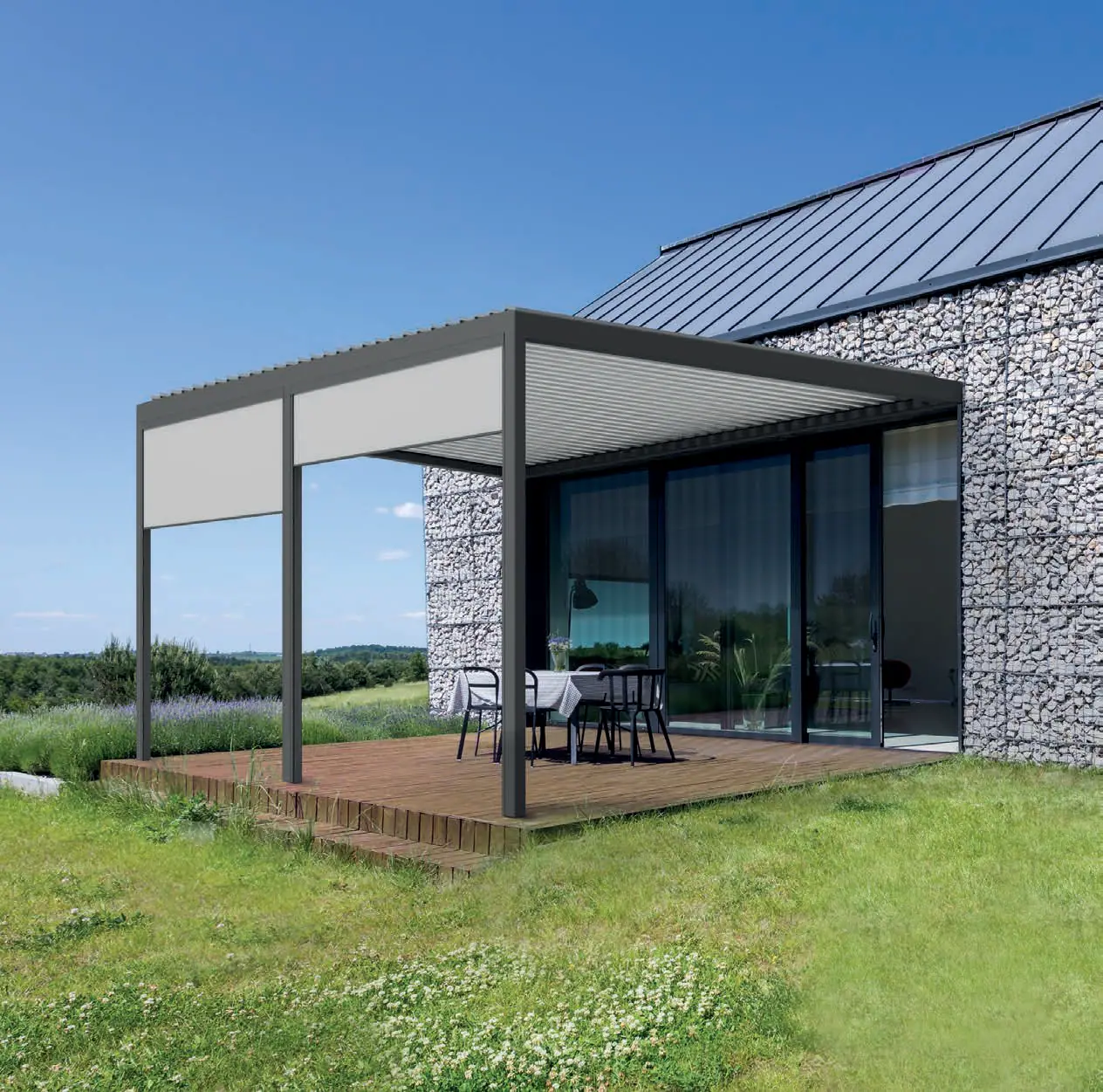 Antracytowa pergola z lamelami przy domu z elewacją z kamienia, od strony ogrodu dwie rolety zip screen opuszczone do połowy, pod dachem stół z krzesłami
