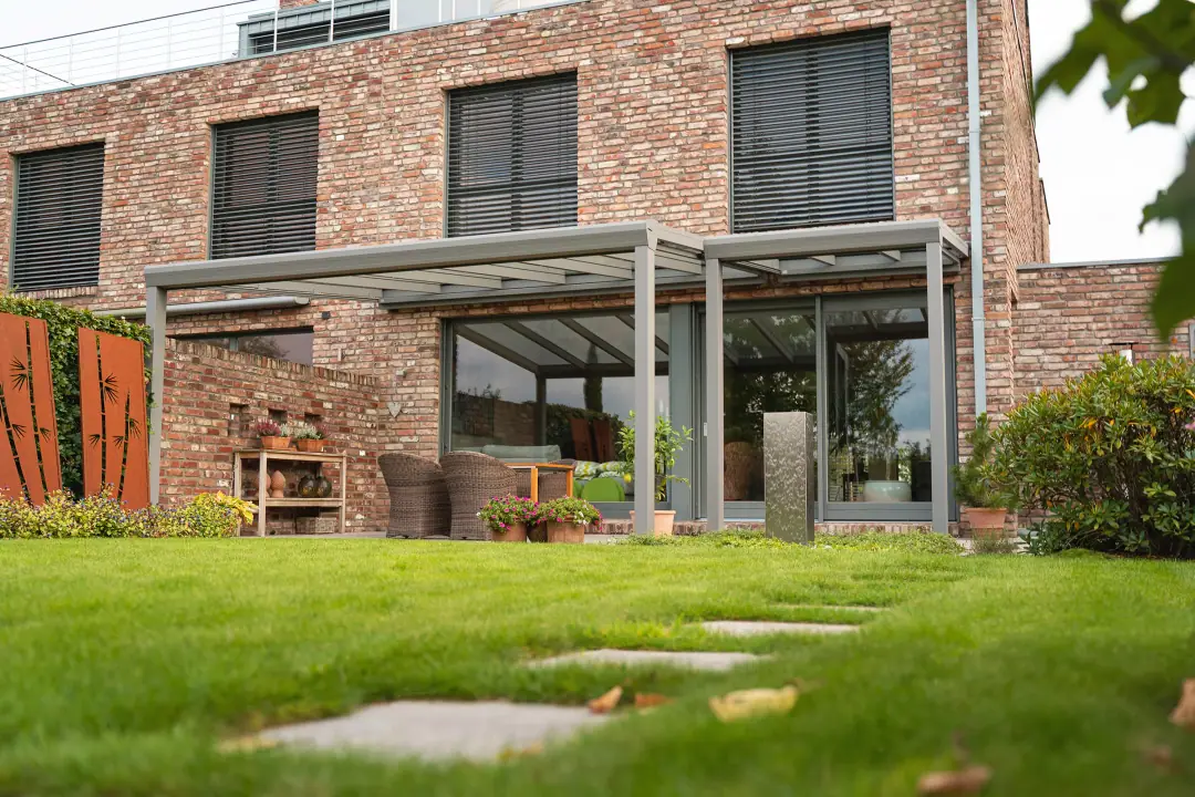 Topstyle w kolorze szarego aluminium przy ceglanym domu, zabudowany szkłem, widok z trawnika