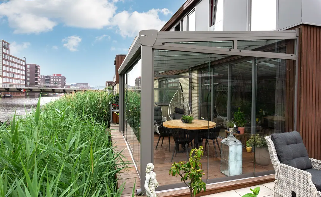 Topstyle w kolorze szarego aluminium ze ścianami panoramicznymi nad kanałem, z jadalnią i fotelem wiszącym