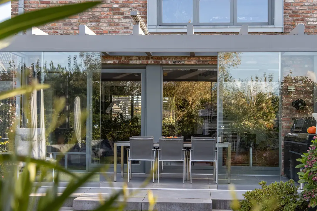 Ultrastyle Compact w kolorze szarego aluminium ze ścianami panoramicznymi i markizą naddachową przy domu z cegły